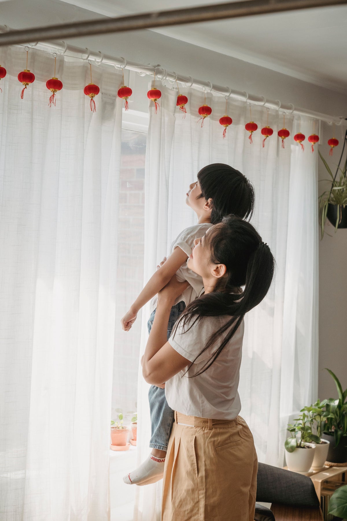 An Asian mother holding her child in a warm interior with red lanterns in the background